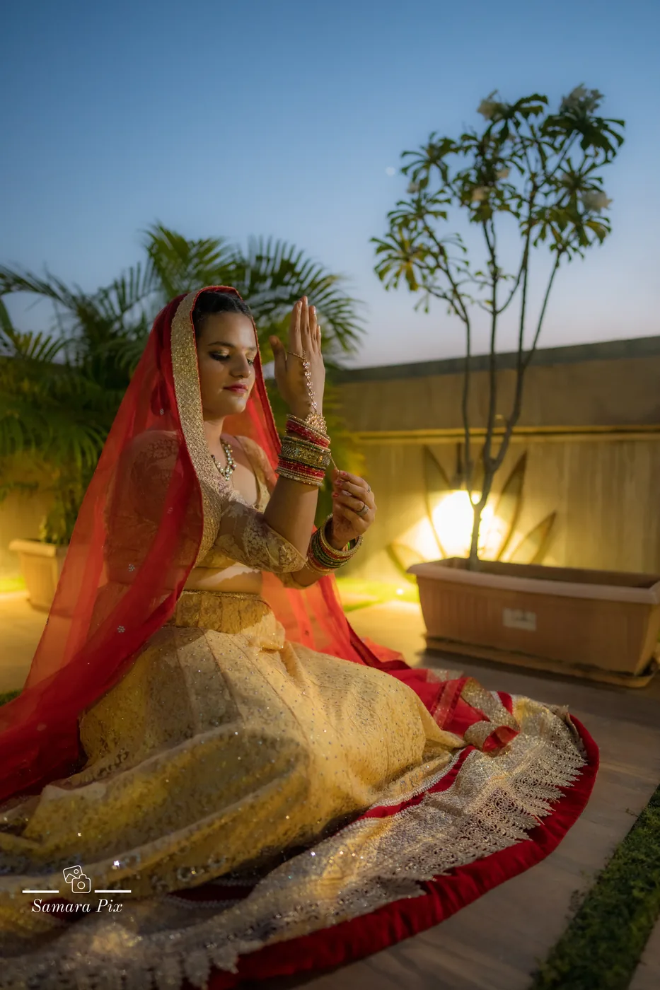 Bride praying under her veil at dusk among garden lights