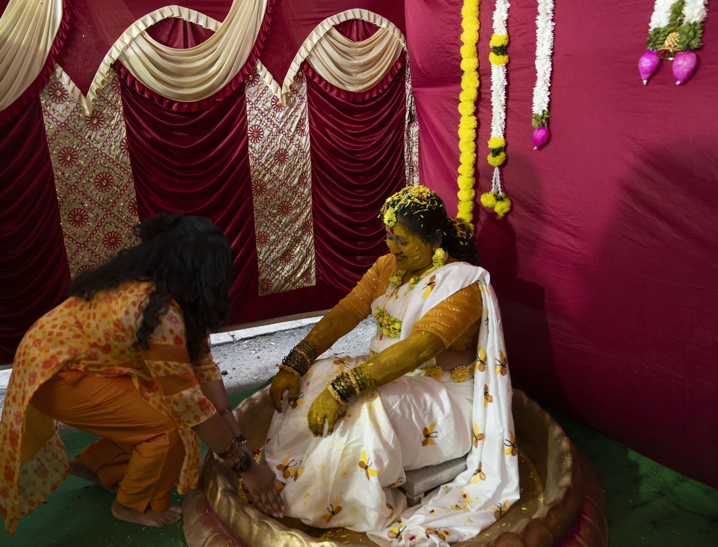 Candid haldi ceremony moment against a red backdrop with marigolds