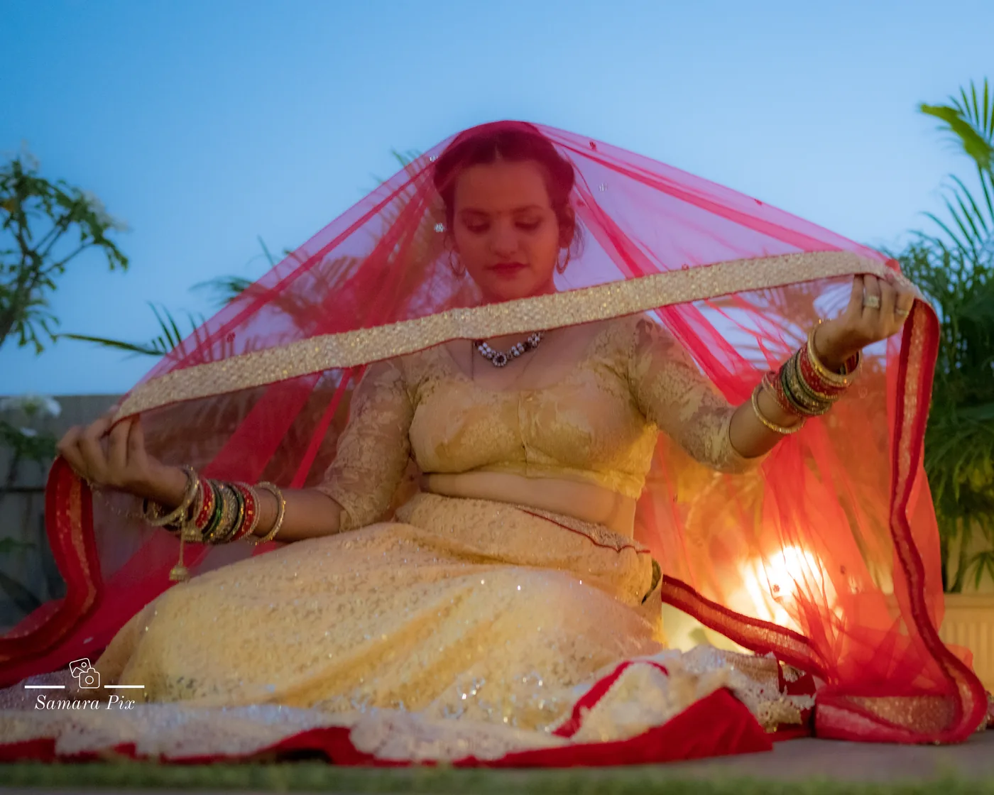 Bride in a yellow lehenga lifting her red dupatta veil